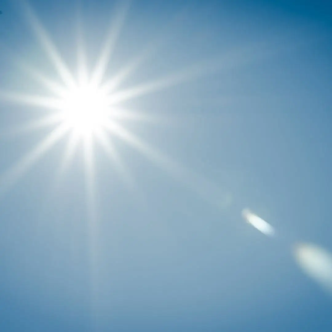 A bright sunlight shining over a lush green field with clear blue skies.